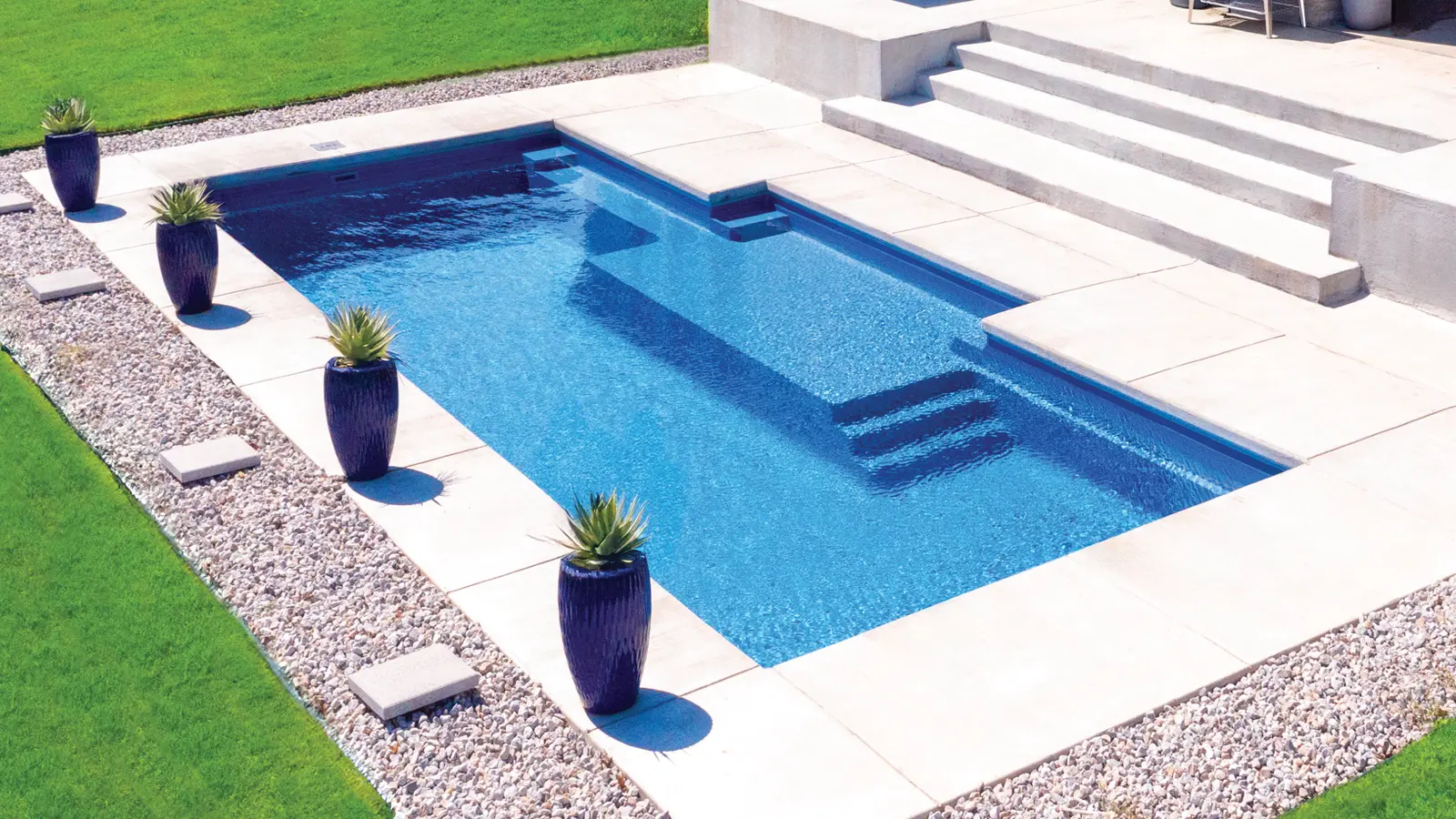AvivaPools_inset02_2026 Aerial view of an Aviva Pools rectangular fiberglass pool with deep navy finish, surrounded by decorative planters and a clean concrete deck