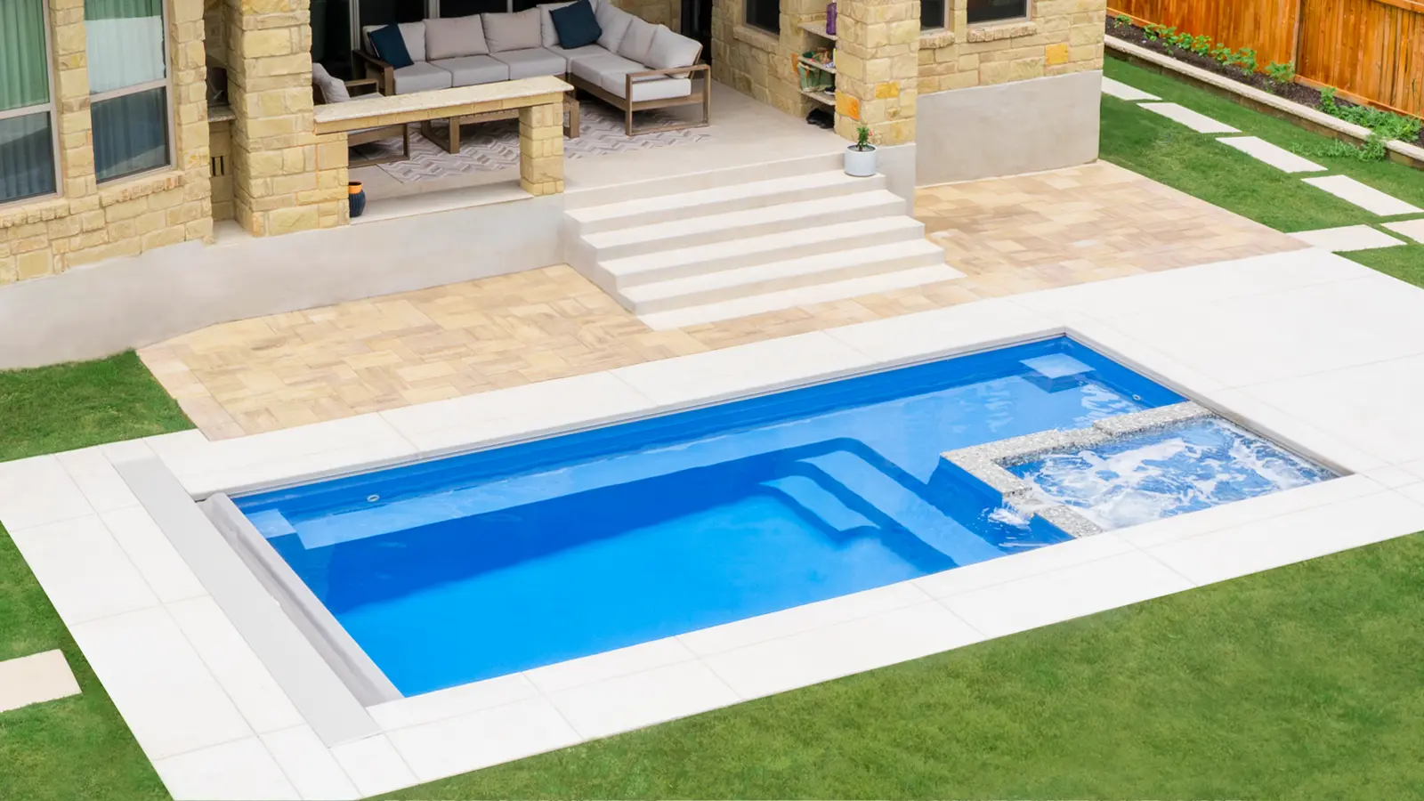 AvivaPools_inset03_2026 Overhead view of an Aviva Pools fiberglass pool with automatic cover and attached spa, installed beside a luxury stone-facade home