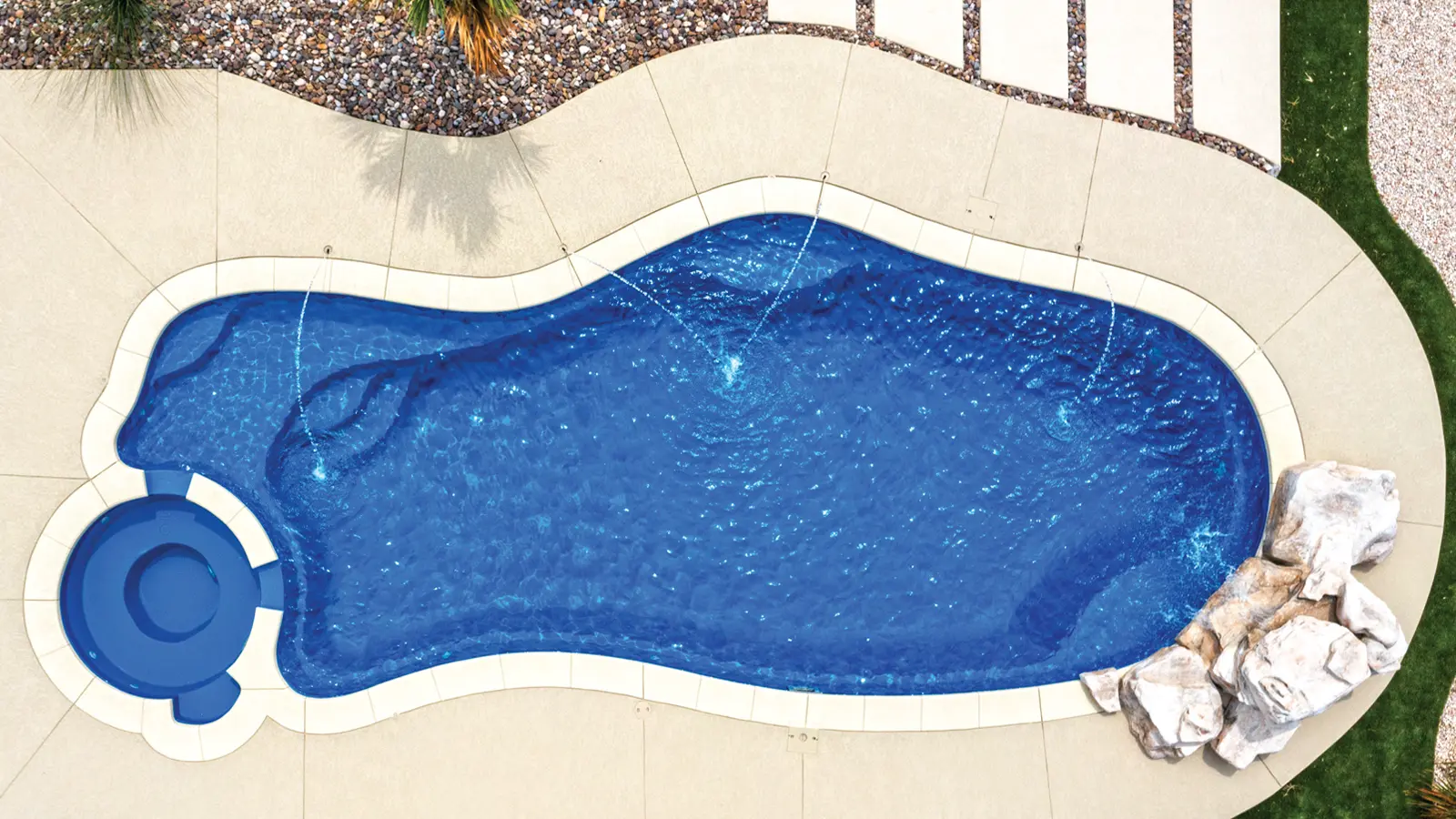 AvivaPools_inset08_2026 Aerial view of an Aviva Pools freeform lagoon-shaped fiberglass pool with circular spa and boulder accent, set in a desert-inspired landscape