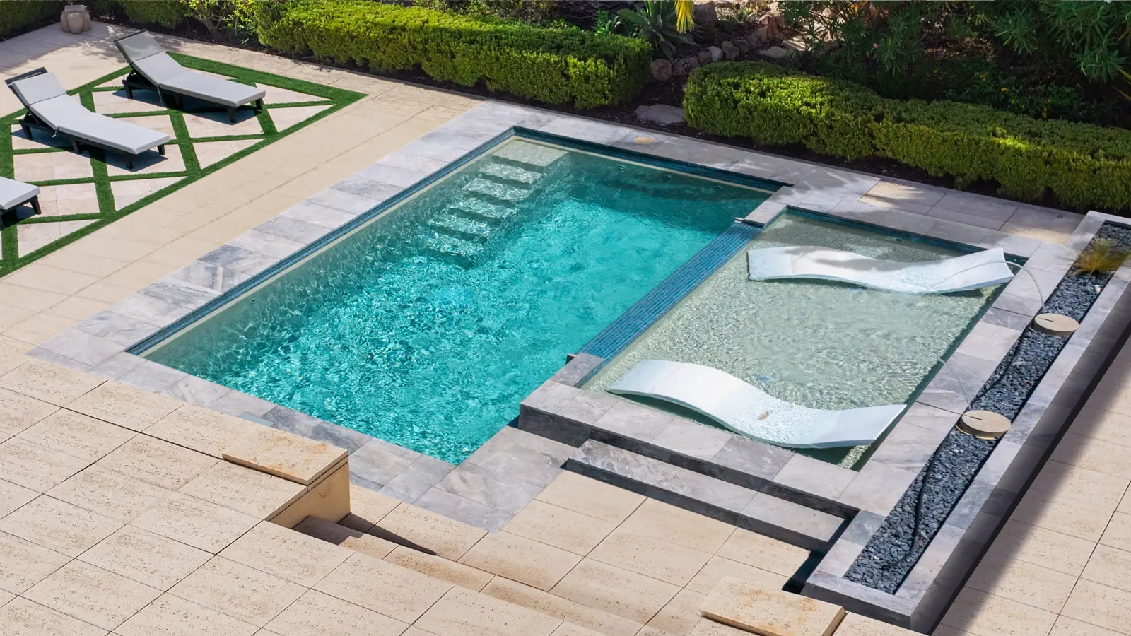 AvivaPools_inset09_2026 Aviva Pools geometric fiberglass pool with expansive tanning ledge and modern sun loungers, framed by a travertine surround and formal garden hedges