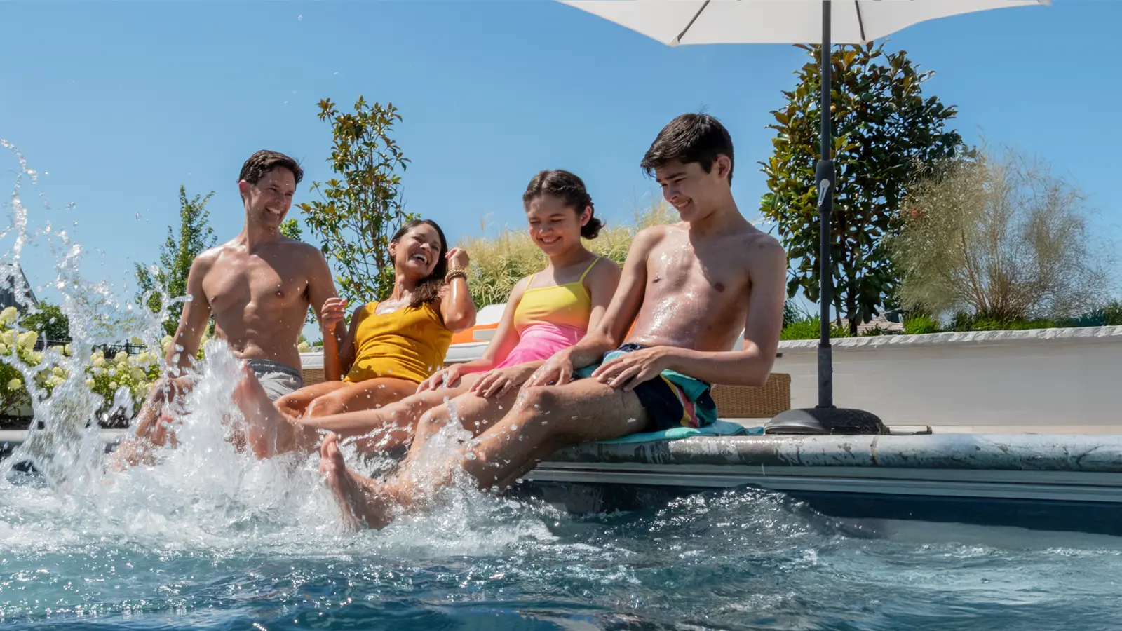 HeroImage_Aviva_2026 Family enjoying an Aviva Pools fiberglass pool on a sunny day, splashing and laughing at the pool's edge